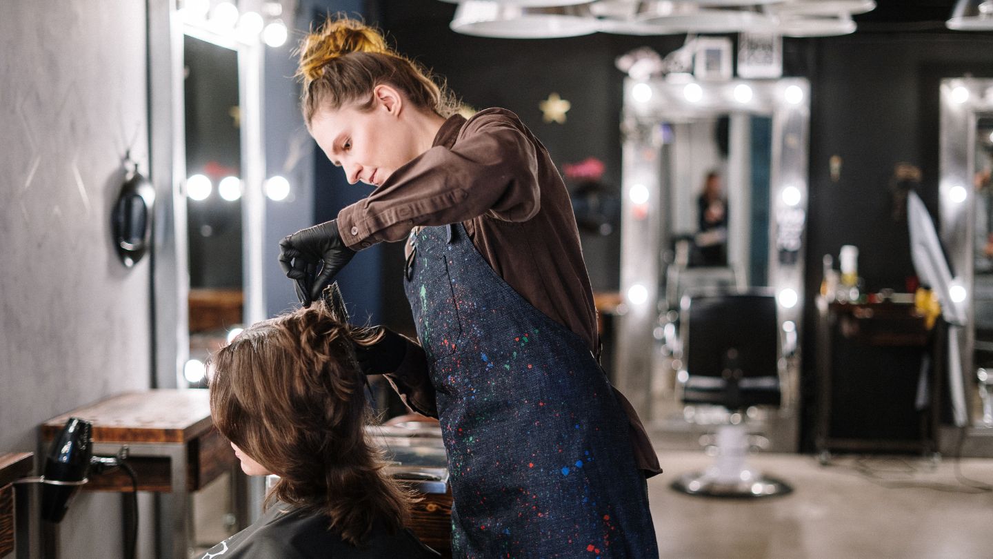 Ambiance chaleureuse et détendue d'un salon de coiffure, avec une coiffeuse experte en train de réaliser un balayage sur une cliente ravie.