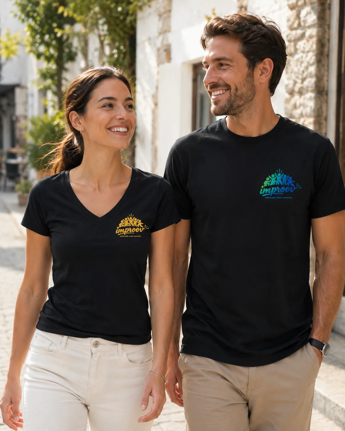 Un homme et une femme souriants portent des t-shirts noirs personnalis&eacute;s dans une ambiance ext&eacute;rieure lumineuse et naturelle. Les mod&egrave;les pr&eacute;sentent un col rond homme, un col V femme et deux marquages color&eacute;s c&ocirc;t&eacute; c&oelig;ur.